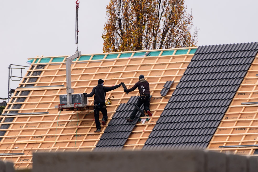 Professional home inspector in uniform, holding a clipboard and carefully examining the shingles and flashing on a new res...
