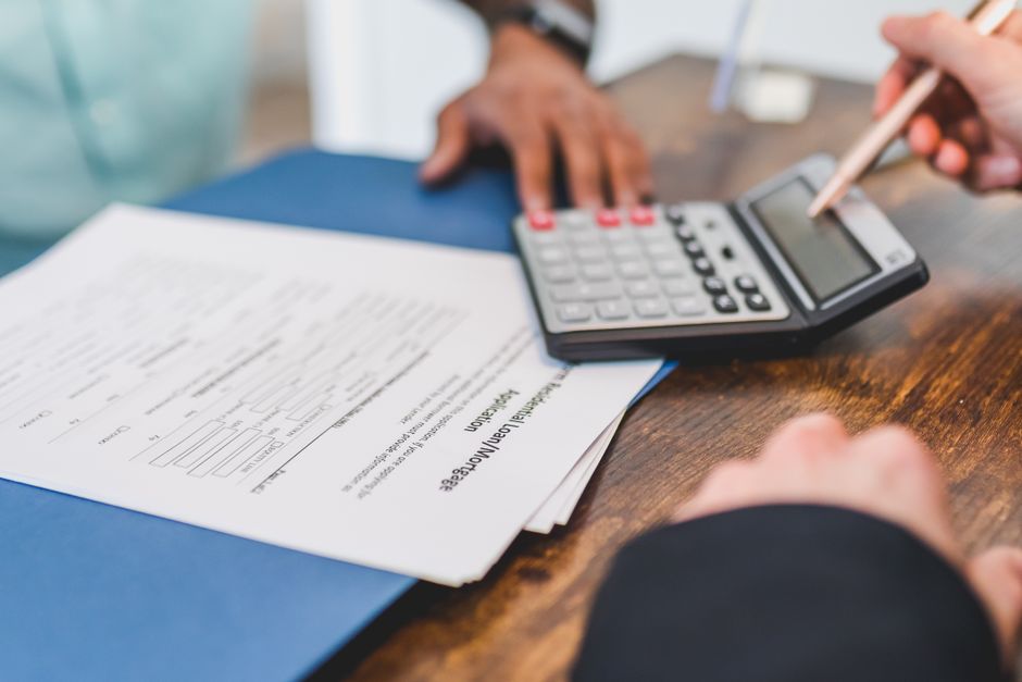 Close-up of a person's hands holding a small model house in one hand and a calculator in the other, symbolizing the financial decisions and calculations involved in maximizing home equity.