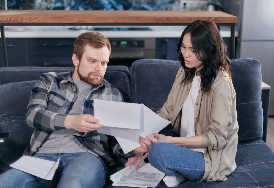 A happy couple sits together on a sofa in a bright, modern living room, reviewing paperwork and smiling, representing an empowered and informed decision about selling their home.